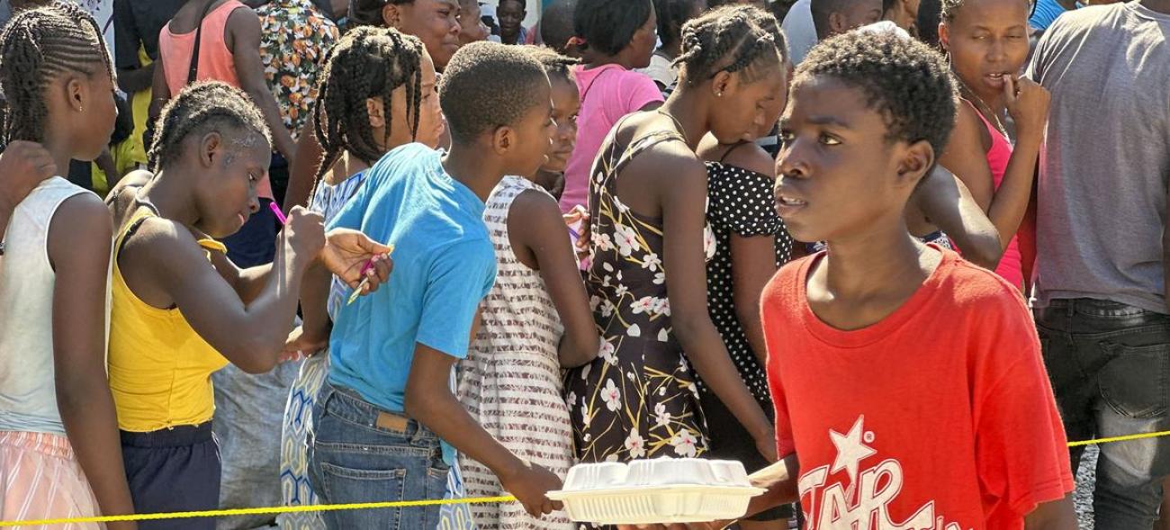 Des enfants haïtiens font la queue pour recevoir un repas chaud et de l'eau distribués par le PAM à Port-au-Prince.